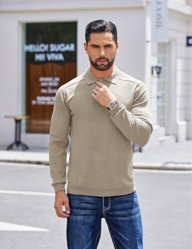 Man wearing a beige sweater and jeans in an urban setting.