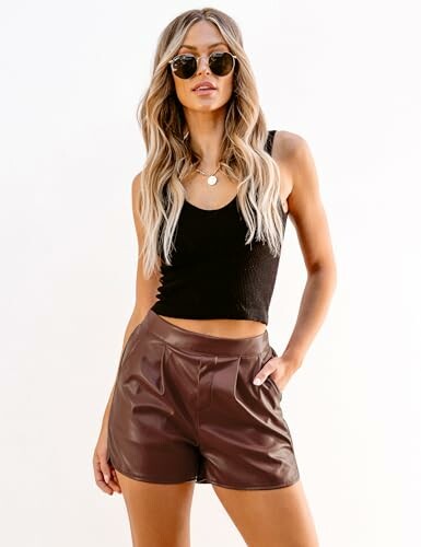 Woman wearing sunglasses, black top, and leather shorts.